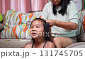 A warm and candid moment of a mother braiding her daughter's hair while the little girl smiles brightly at home. 131745705