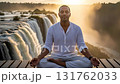 Calm man practicing yoga and meditation in lotus pose at sunrise in front of a big waterfall 131762033