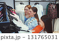 Three young women browsing clothes on hangers in fashion store, choosing stylish outfits together and enjoying shopping experience 131765031
