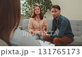 Distressed couple on sofa in therapy session, woman crying into tissue, man holding her hand, therapist listening in foreground 131765173
