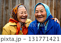 A heartwarming medium shot of two happy elderly Asian women in colorful headscarves laughing together outdoors 131771421