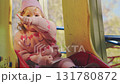 A happy toddler in a pink sweater slides down a playground slide, laughing with joy. The setting features green trees and colorful play equipment, showing a typical day at the park. 131780872