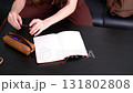 A woman's hand sits at a table, takes a pen from a pencil case, and writes in a notebook with her left hand. A left-handed woman in a red T-shirt opens a notebook and writes down her plans. 131802808