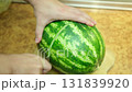 A man cuts a watermelon in half, showing its ripeness at the end. 131839920