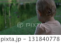little girl with short curly blond hair happily looking at birds and fish in a big lake in a city park, not moving 131840778
