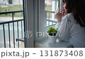 Embracing the Gray Skies: Woman Taking a Joyful Coffee Break by the Window 131873408