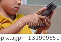 Close-up of an Asian child playing a mobile game on smartphone at home, showing modern lifestyle, technology use, and digital entertainment among kids today. 131909651