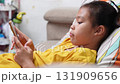 Close-up of an Asian child playing a mobile game on smartphone at home, showing modern lifestyle, technology use, and digital entertainment among kids today. 131909656