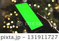 Girl Holds A Smartphone With A Chroma Key Green Screen Against A Background Of Christmas Lights 131911727