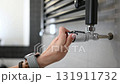 Female Hand Adjusts The Temperature Of The Radiator of Towel Warmer In The Bathroom 131911732