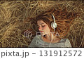 A girl with headphones lying on the hay.  A young woman listening to music lying. 131912572