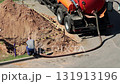 pumping tank against the background of a pit with a fence. Concept of liquidation of an emergency breakdown in a water supply system, copy space for text. A male worker operates a hose to pump out a 131913196