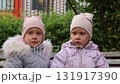 Two little twin sisters kissing on a bench 131917390