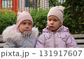Two little twin sisters kissing on a bench 131917607