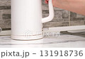 A woman's hand turns on a white electric kettle with a button 131918736
