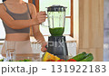 Smiling woman preparing a healthy green smoothie in a blender in a kitchen 131922183