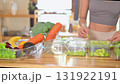 Woman organizing sliced fruits and fresh vegetables into meal containers on a wooden kitchen counter 131922191