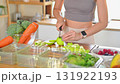 Young woman slicing green apples on a cutting board surrounded by fresh fruits and vegetables. Concept of weekly meal prep 131922193