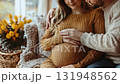 A joyful couple embracing and anticipating the arrival of their baby while seated comfortably in a cozy living room. 131948562