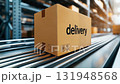A brown cardboard box with the word delivery placed on a conveyor belt in a modern warehouse setting. 131948568