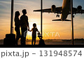A family watching an airplane take off at sunset from the airport terminal window. 131948574