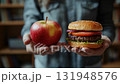 A person choosing between a healthy apple and a tasty hamburger while holding both in hands. 131948576
