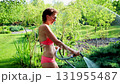 Young adult sexy slim sporty caucasian brunette woman enjoy having fun watering garden at home yard with hose pipe shower on hot summer day. Happy female person relax at backyard park outdoors 131955487