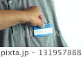 A hand is attaching a blue and white visitor tag on a visitor's pocket. It is a casual gray shirt with a button-down collar. 131957888