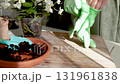 Woman wearing gloves tends to potted flowers on sunny day. Gardening tools on table. Nature and plant care. Interior design. 131961838