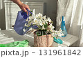 Woman waters potted flower with watering can on sunny day. Gardening tools on table. Nature and plant care. Interior design. 131961842