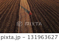 Aerial view of a tractor plowing a vast field during sunset, leaving even furrows in the soil. Agricultural machinery working in rural farmland in golden light. 131963627