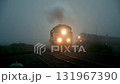 Wide shot of a train with bright headlights approaching on railroad tracks through thick atmospheric fog 131967390