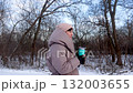 A woman in a warm down jacket drinks hot tea from a thermal cup in the winter forest 132003655