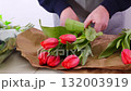 Florist arranging fresh red tulips in brown paper bouquet with careful hands 132003919
