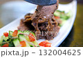 Serving of sliced boiled beef tongue with pickled cucumbers and bell peppers drizzled with olive oil soy sauce and crushed garlic topped with black and white sesame and microgreens on white plate. 132004625