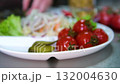 Process of preparing traditional pickled vegetables sliced cucumbers placed beside salted tomatoes plate with jar of marinated mushrooms creating healthy homemade appetizer rich in natural probiotics 132004630