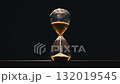 Close-up photograph of golden glittering sand leaking out of an hourglass. 132019545