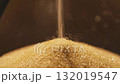 Close-up photograph of golden glittering sand leaking out of an hourglass. 132019547