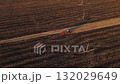 Aerial view of a red tractor plowing the field after harvest at sunset in autumn. Farming machinery working on farmland, golden light rural landscape. 132029649