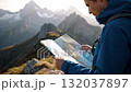 A man in a blue jacket looking at a map in the mountains 132037897