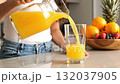 A woman pouring orange juice into a glass of orange juice 132037905