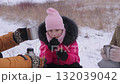 Girl in warm outfit eats cookie and mother adjusts hat at countryside in winter 132039042