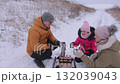 Young active family warms with hot tea and biscuits on sledge in winter field 132039043