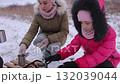 Mother and daughter arrange snacks on sledge father pours hot tea on winter day 132039044