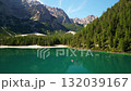 Aerial view of a turquoise alpine lake, lush pine forest, and rugged mountain peaks 132039167