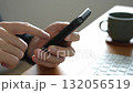 A man operating a black smartphone with his right hand on a wooden desk 132056519