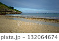 Low-angle view of a beach on Belle-ile-en-Mer on a sunny summer day with waves rolling onto the shore. There are boats anchored in the distance on the sea. 132064674
