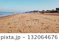 Low-angle view of a beach with dunes. The waves of the sea reach the beach during a sunny autumn day. People are walking and running on the beach. In the distance, you can see apartments and house on 132064676