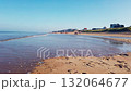 Low-angle view of a beach with dunes. The waves of the sea reach the beach during a sunny autumn day. People are walking and running on the beach. In the distance, you can see apartments and house on 132064677