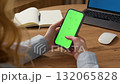 Woman sit use digital tech cell phone, green screen mock up. Hand scroll phone web site, swipe like photos. Girl hold mobile closeup. Chroma key page. Cozy office background. Online app copy space. 132065828
